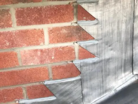 New lead step flashing dressed into brickwork beside a slate roof