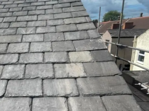 Roofer repairing a slate roof, with replacement slates fitted alongside the originals